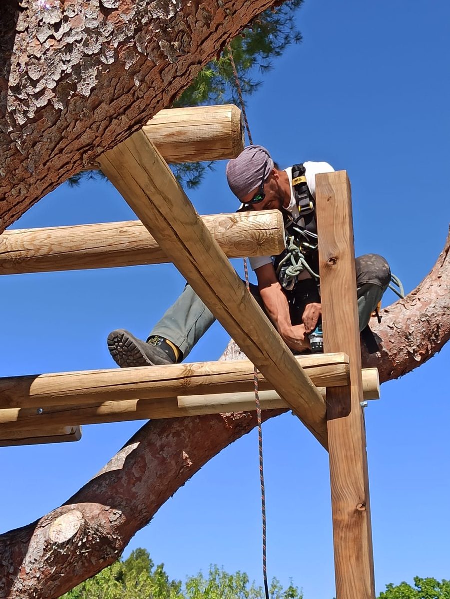 Gabriel en train de construire une structure en bois sur poteau, en hauteur
